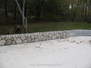 Travertine stone patio with veneered stone sitting wall and fire pit.